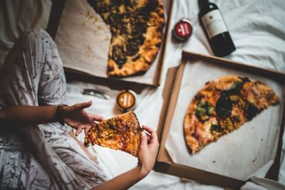Overview of person having pizza from Pizzeria Tra Vigne on guest room bed
