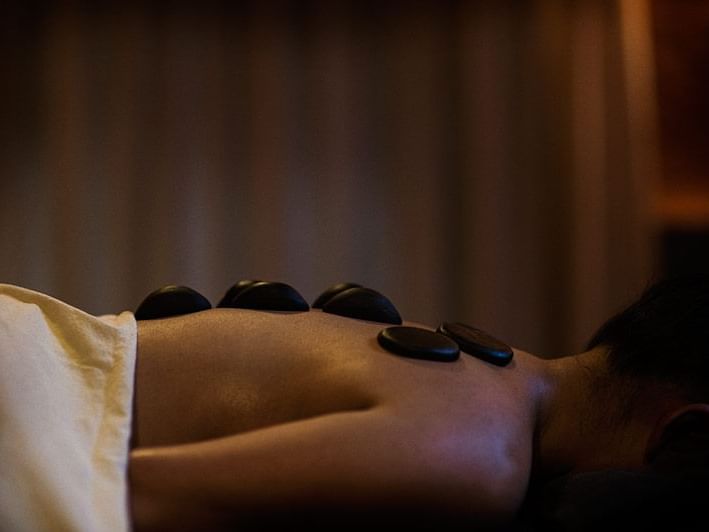 Lady receiving a hot stone massage with smooth black stones in the spa at Dwarika's Himalayan Wellbeing