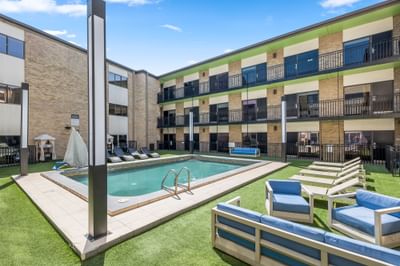 Sunny courtyard at Riverwalk Plaza Hotel with a swimming pool, lounge chairs, multi-story buildings, and green grass