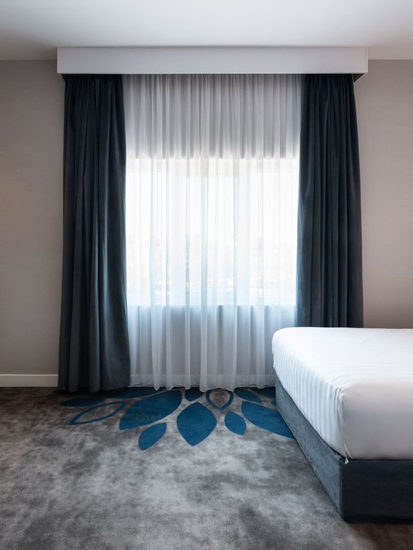 Twin beds by a wooden desk and a round stool on a grey and blue floral carpet in Royal Suite Sea View at Warwick Al Jubail