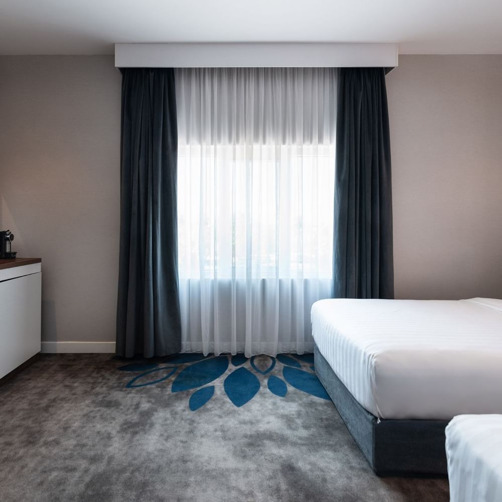 Twin beds by a wooden desk and a round stool on a grey and blue floral carpet in Royal Suite Sea View at Warwick Al Jubail