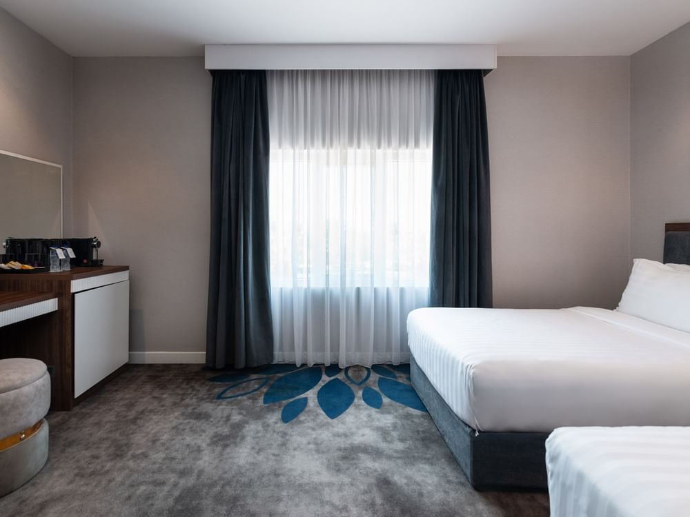 Twin beds by a wooden desk and a round stool on a grey and blue floral carpet in Royal Suite Sea View at Warwick Al Jubail