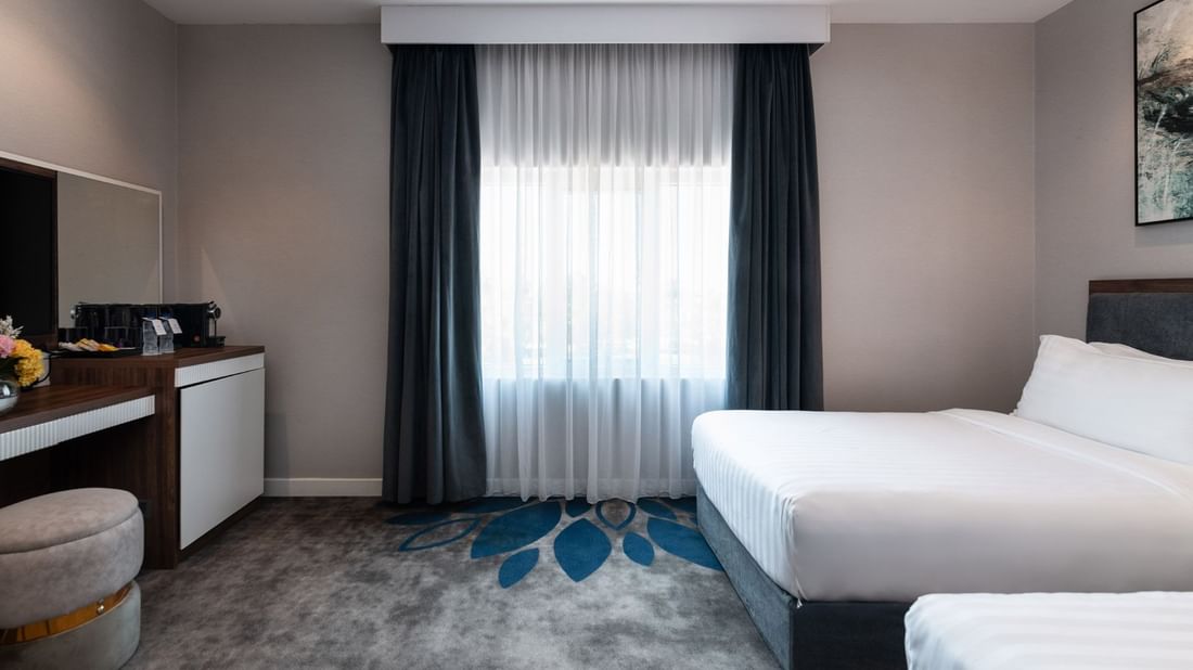 Twin beds by a wooden desk and a round stool on a grey and blue floral carpet in Royal Suite Sea View at Warwick Al Jubail
