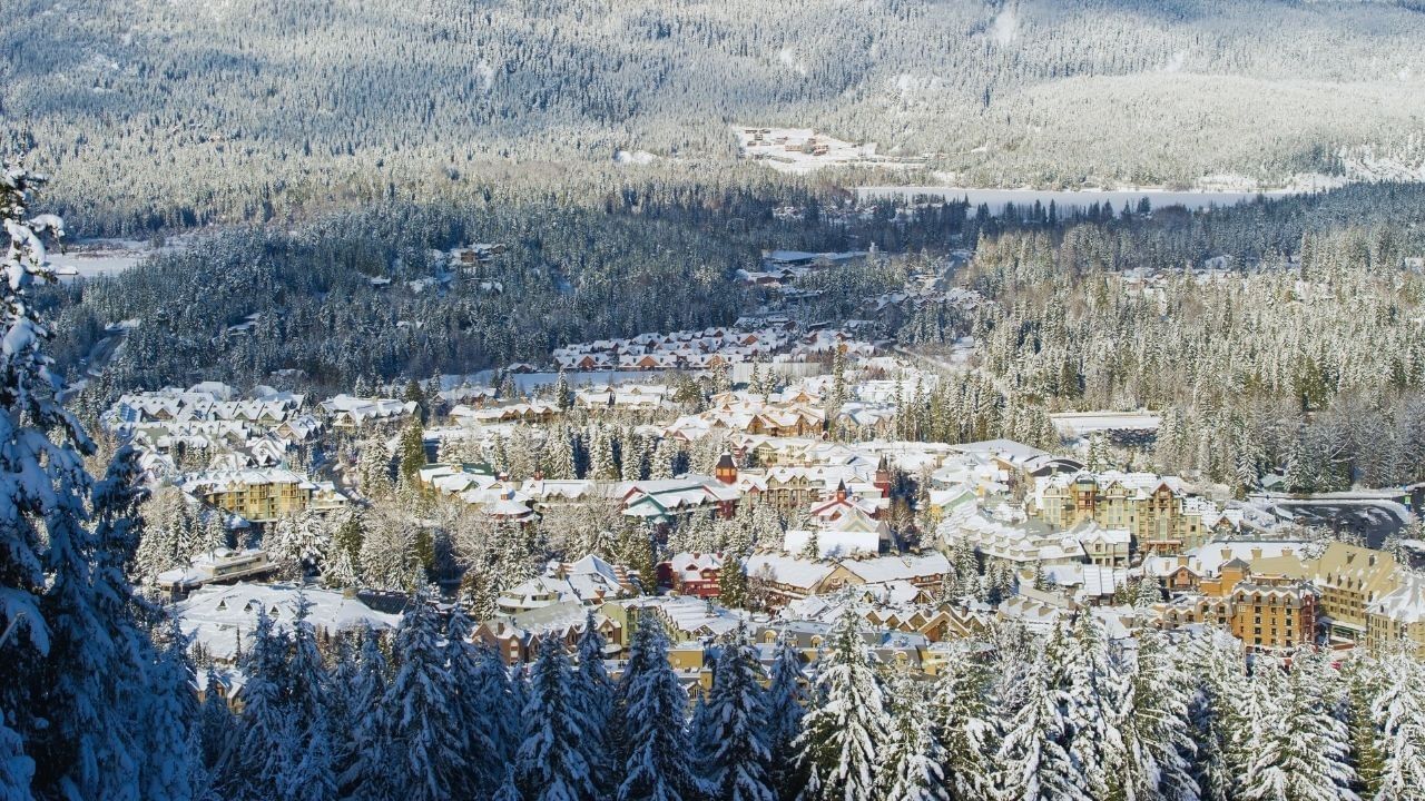 Aerial view of a snowy town nestled in a valley with pine trees and mountains.