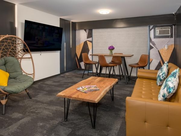 A cozy living room with a brown couch, wicker chair, wooden table and flat-screen TV.