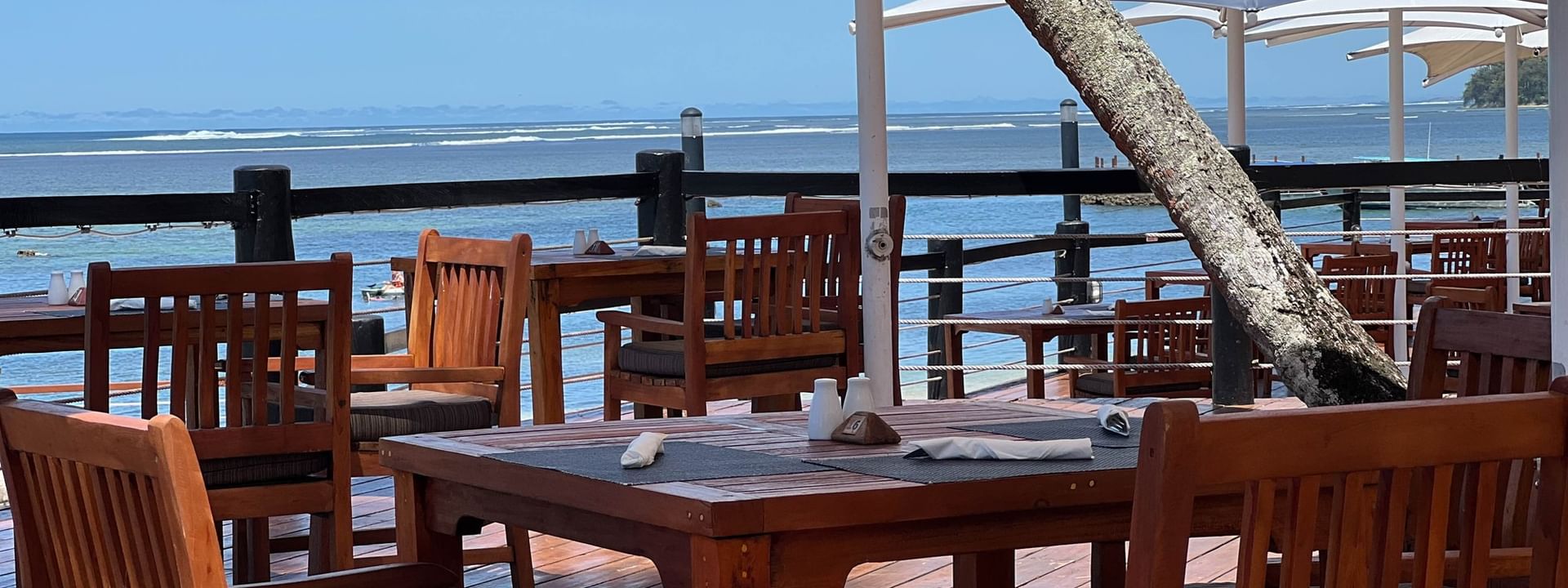 Outdoor dining area with wooden tables and chairs under umbrellas overlooking the ocean at Warwick Fiji Resort and Spa, Korolevu