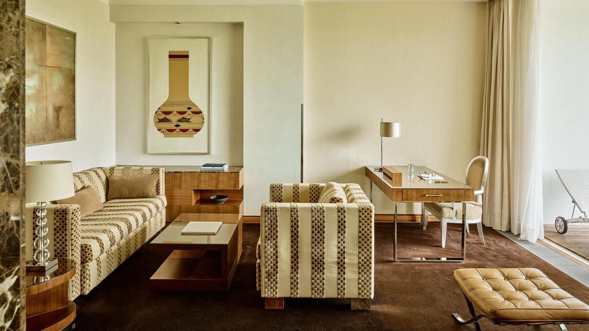 A luxurious living room with striped couches, a desk, and a chair, featuring a large framed artwork.