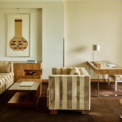 A luxurious living room with striped couches, a desk, and a chair, featuring a large framed artwork.