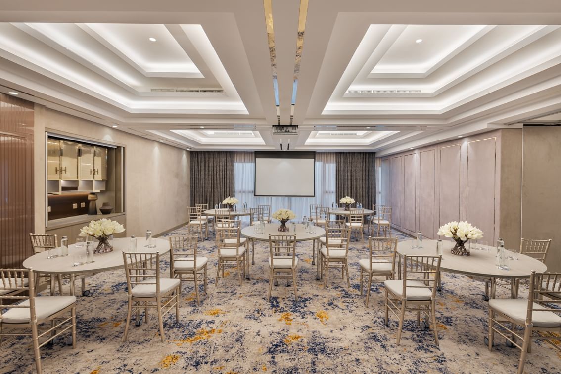Business Studio 3 at Paramount Hotel Midtown with round tables, chairs, and a projector screen in soft ambient lighting