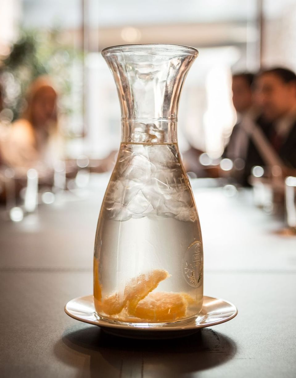 Agua con hielo y rodajas de naranja bajo luz suave cerca de mesa larga en sala de reuniones en NOI Vitacura