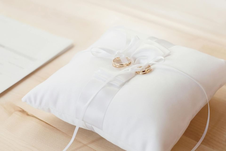 White satin ring pillow with two silver wedding rings tied on a wooden surface at Ananea Madivaru Maldives