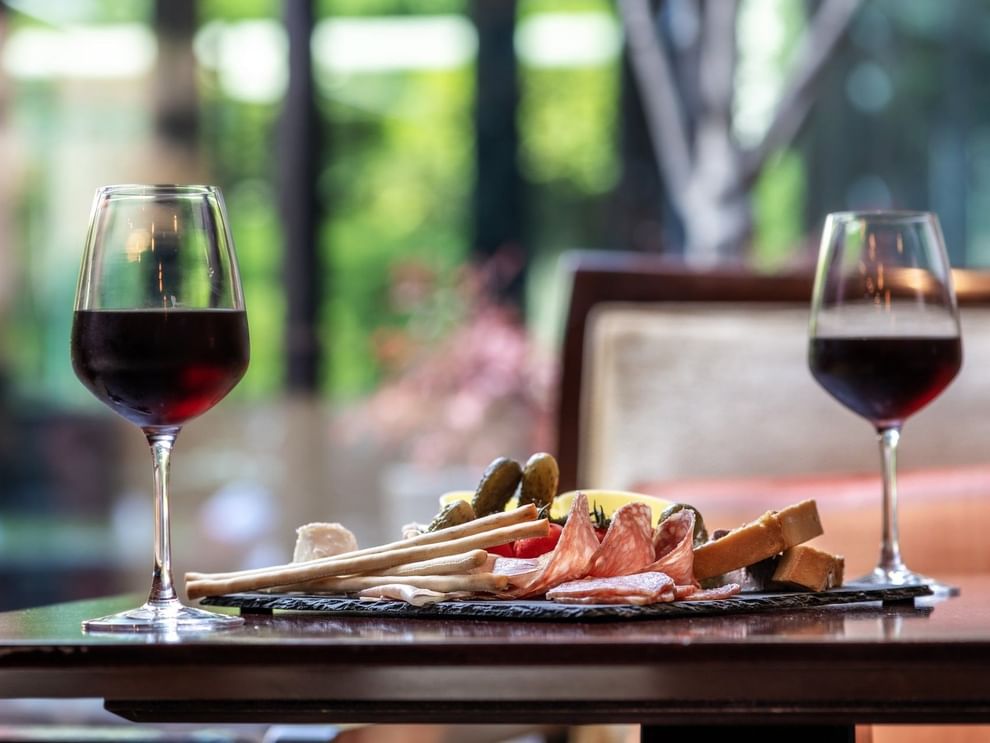 Two glasses of red wine are on a table with a charcuterie board  in The Lounge Bar & Terrace at Warwick Reine Astrid - Lyon