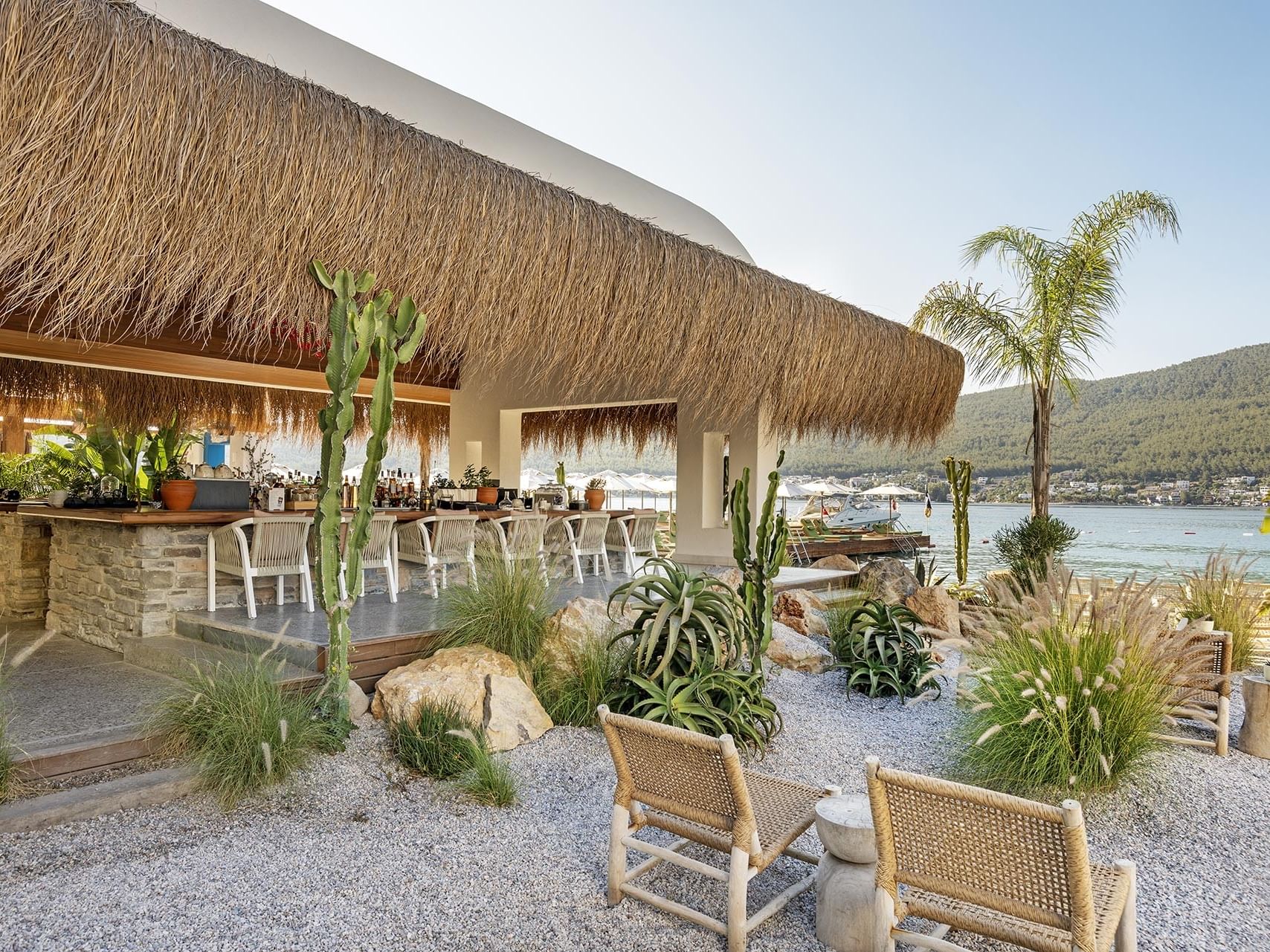 Seaside café with a stone veranda, palm trees, and beach views at Titanic Luxury Collection Bodrum.