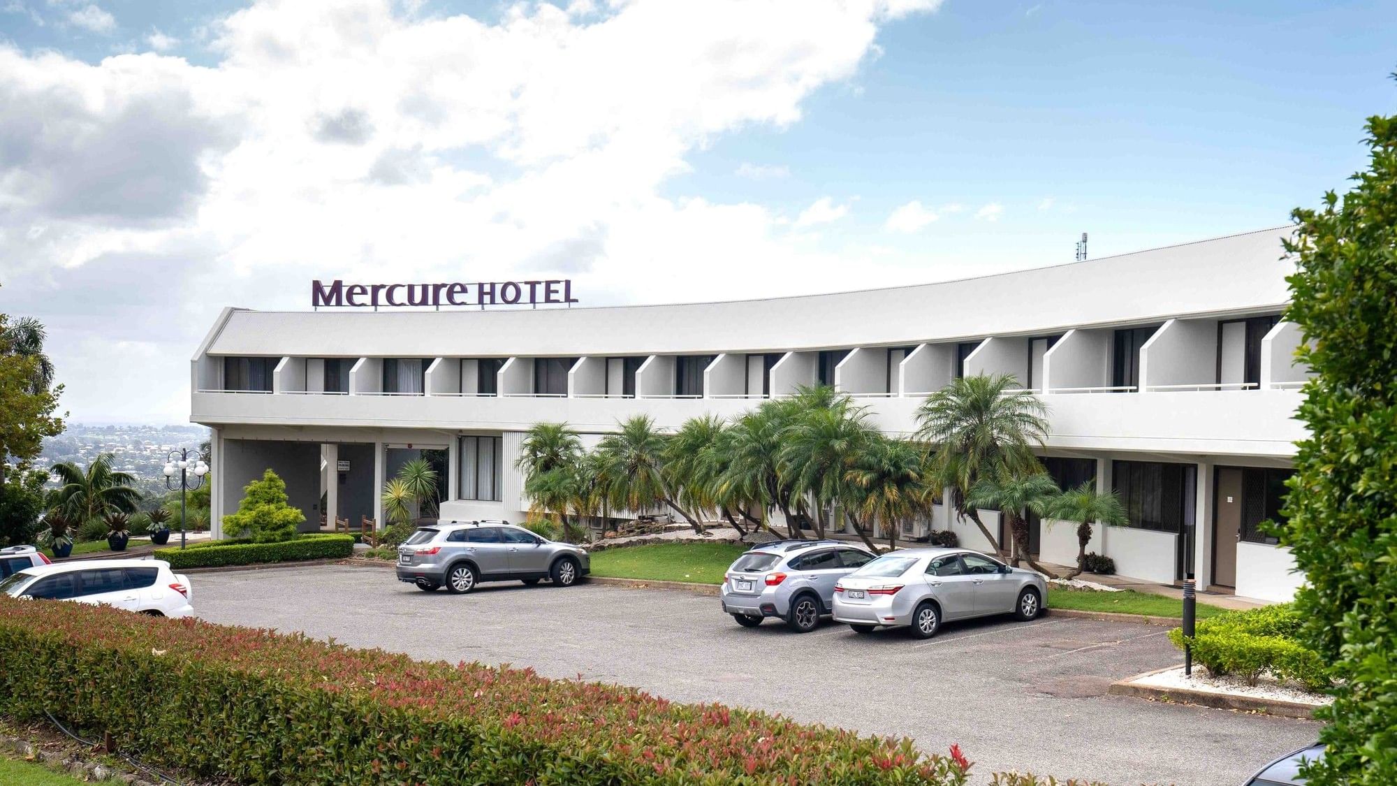 Four cars parked in front of Mercure Hotel in a tropical setting.
