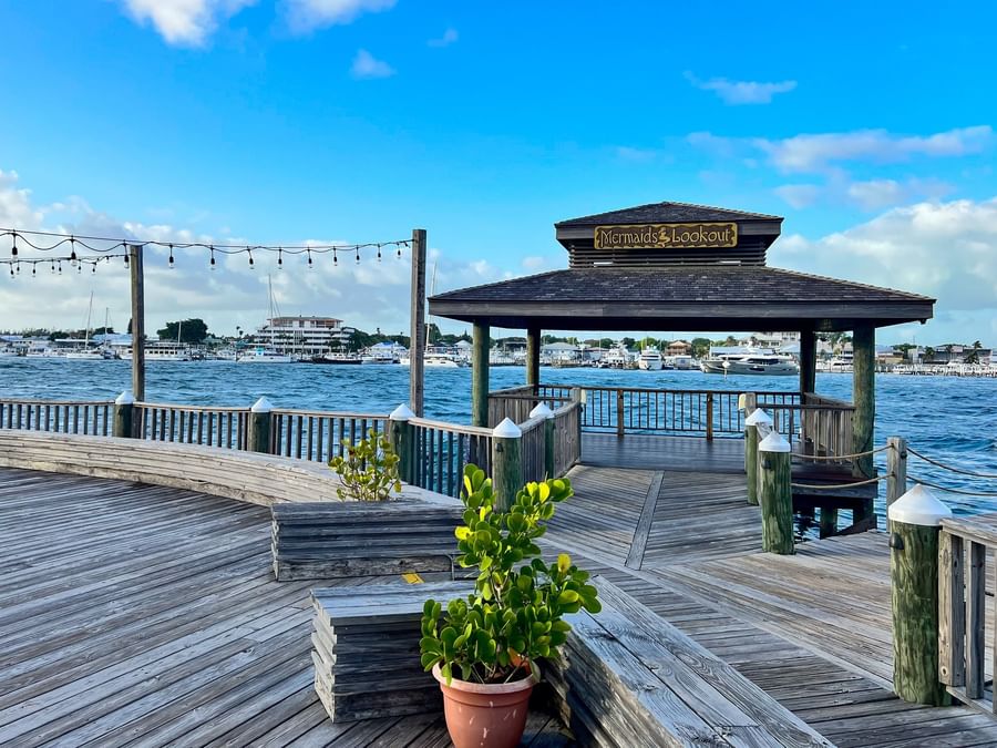 Wooden pier with a shaded gazebo at Warwick Paradise Island Bahamas overlooking a harbor by calm blue water and boats