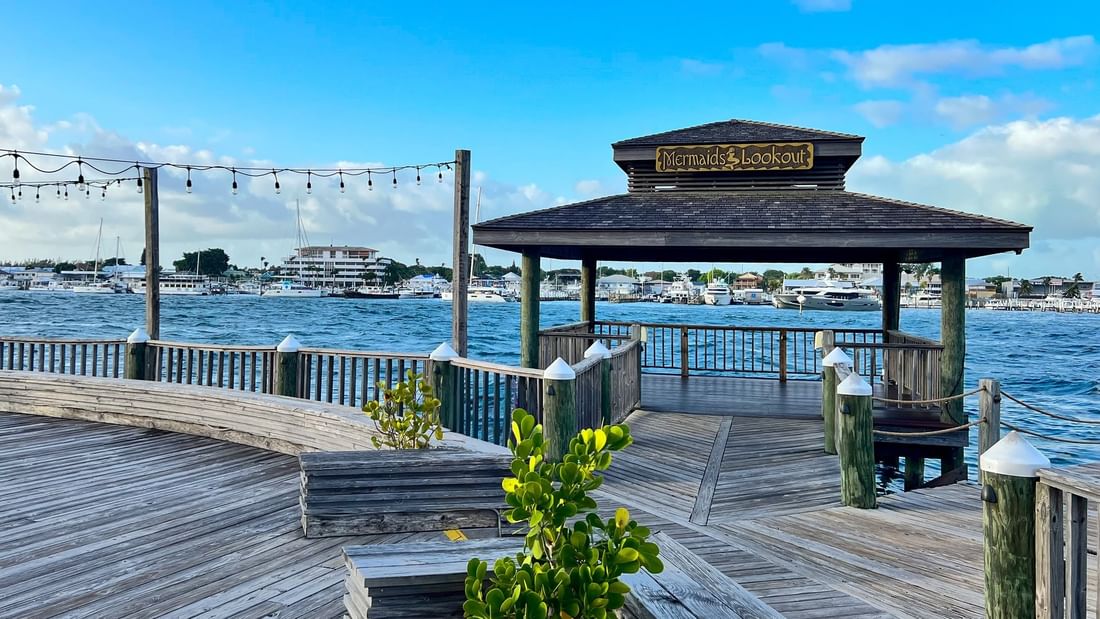 Wooden pier with a shaded gazebo at Warwick Paradise Island Bahamas overlooking a harbor by calm blue water and boats
