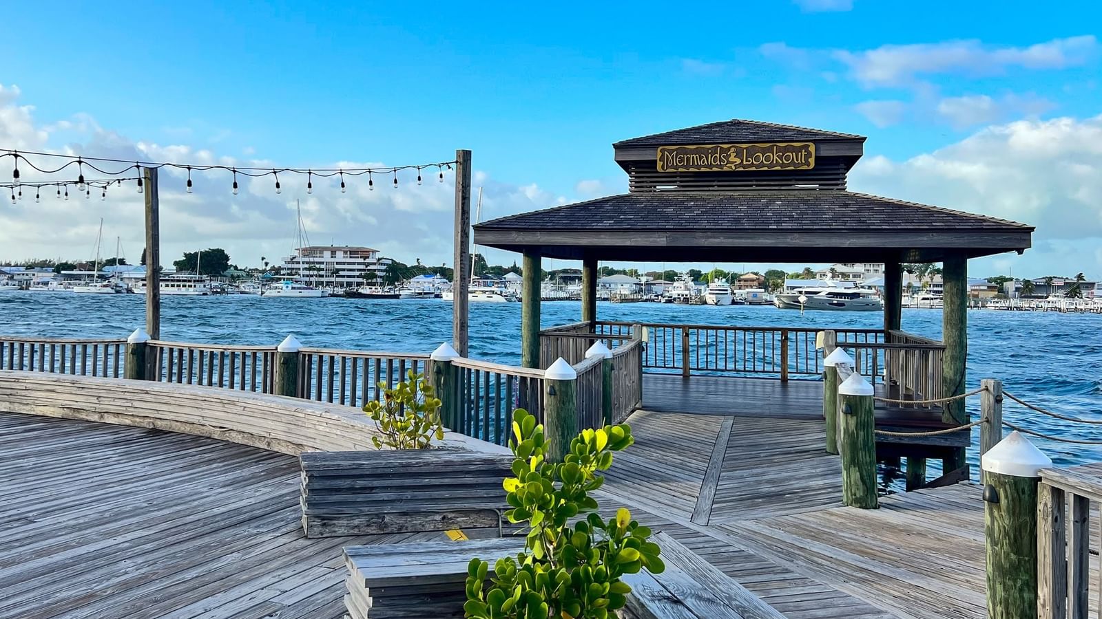 Wooden pier with a shaded gazebo at Warwick Paradise Island Bahamas overlooking a harbor by calm blue water and boats