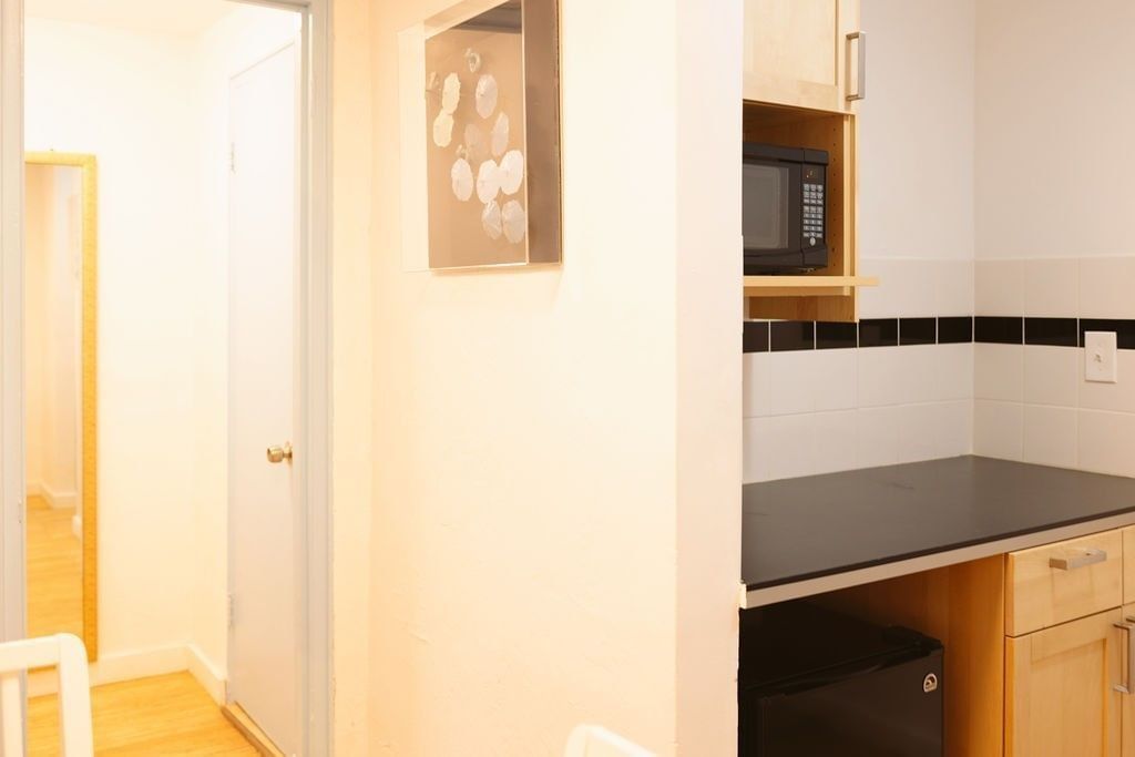 A kitchenette area with a microwave, mini fridge, and cabinets, adjacent to a doorway leading to another room.