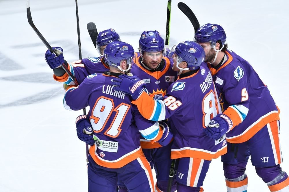 A huddle of hockey players on the ice in purple and orange Orlando Solar Bears hockey gear. 