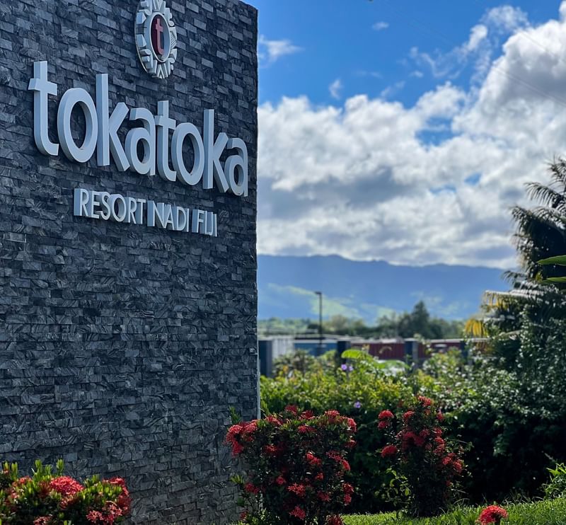 Large resort sign on a stone wall by red flowers and palm trees at TokaToka Resort Nadi Fiji