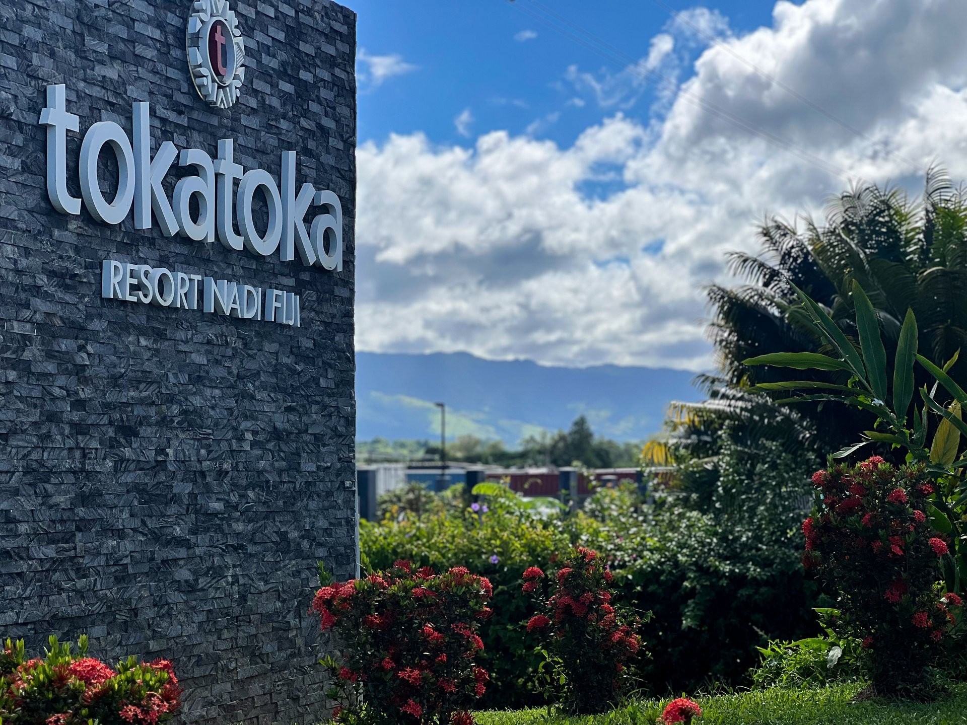 Large resort sign on a stone wall by red flowers and palm trees at TokaToka Resort Nadi Fiji