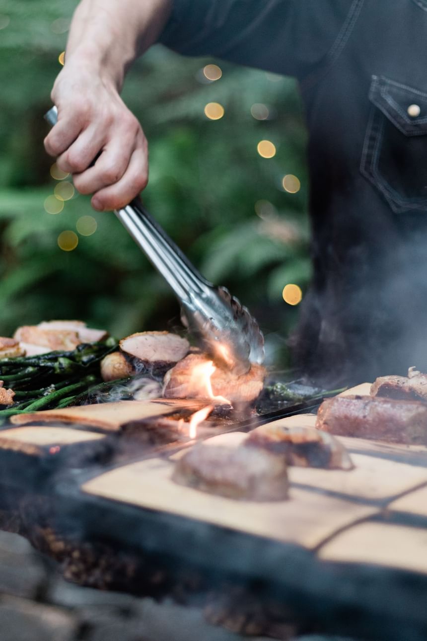 Person grilling meat in an outdoor dining venue at Alderbrook Resort & Spa