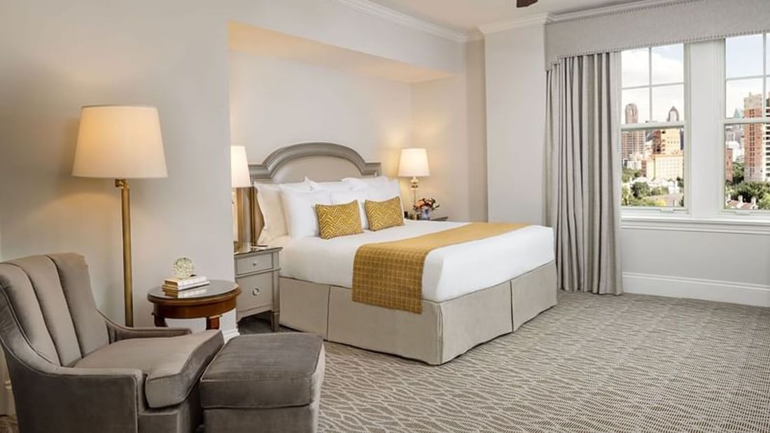 Classic King features King bed by a velvet ottoman under a gold lamp at Warwick Melrose Dallas