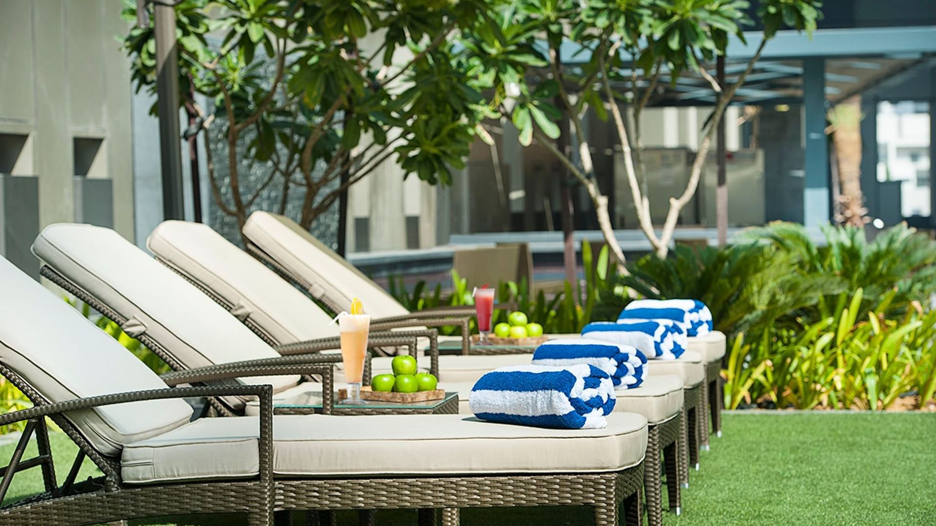 Close-up of pool lounge chairs with towels and fruit served at DAMAC Maison Cour Jardin