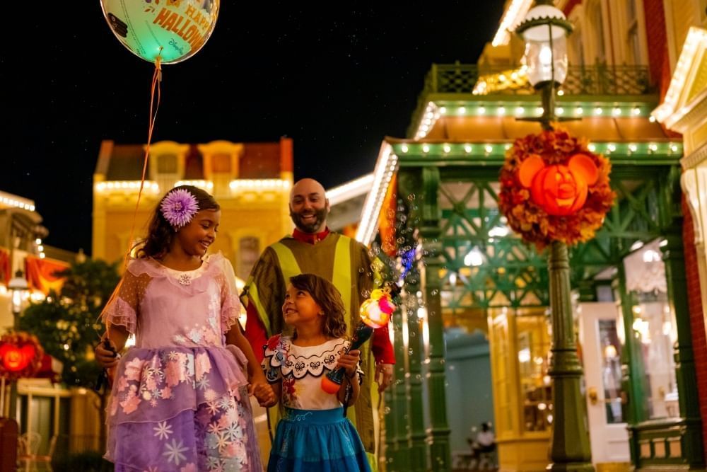 Two girls and their dad dressed as characters from Encanto walk through Main St. USA in Disney World at night.