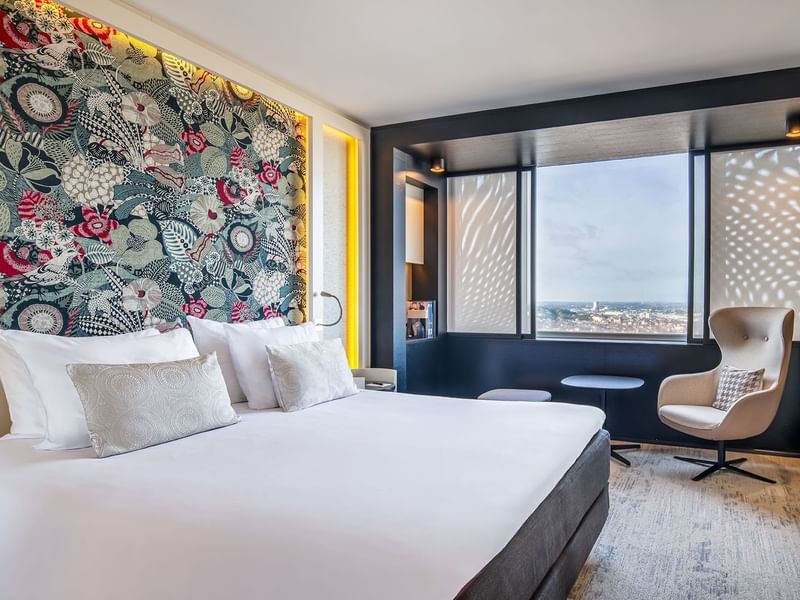 Deluxe Panorama room with a floral wall, large bed, and city view through windows at The Hotel Brussels