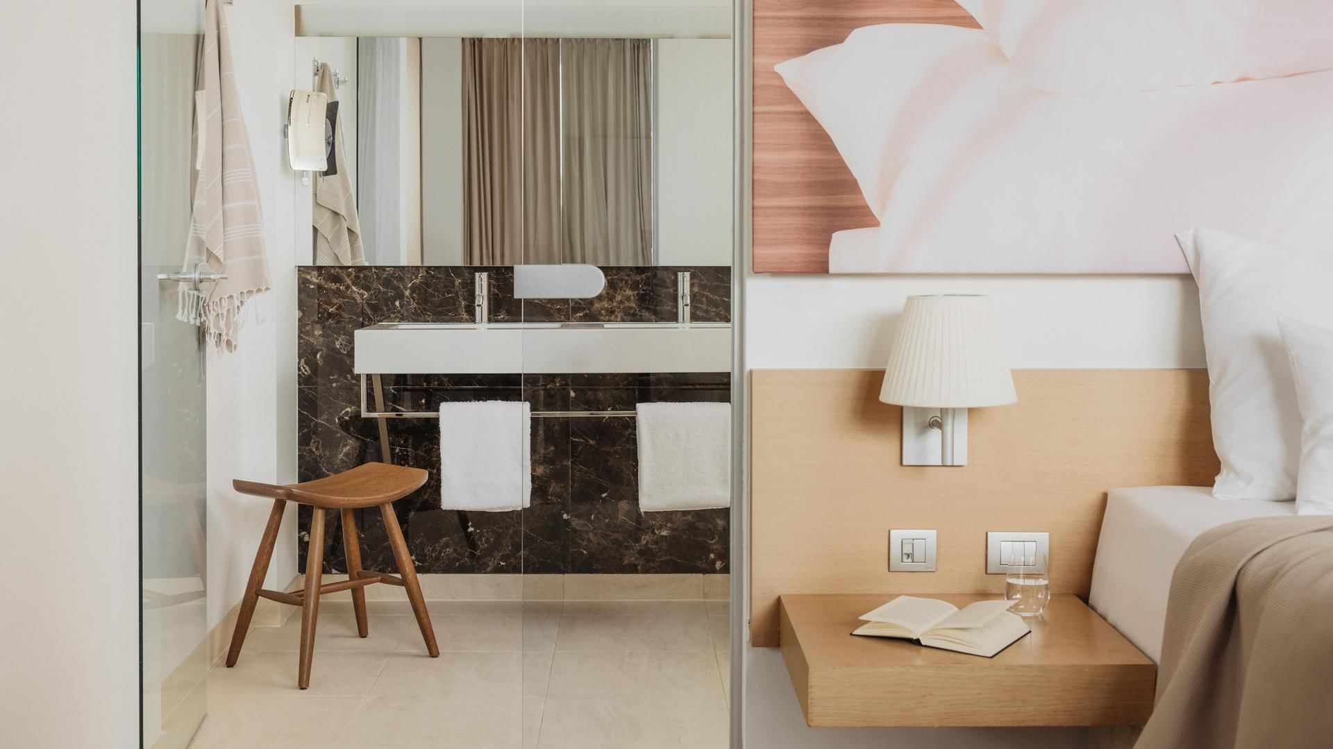 Modernes Hotelzimmer mit sichtbarem Bad, Holzmöbeln und einem Bett mit Kopfteildekoration.