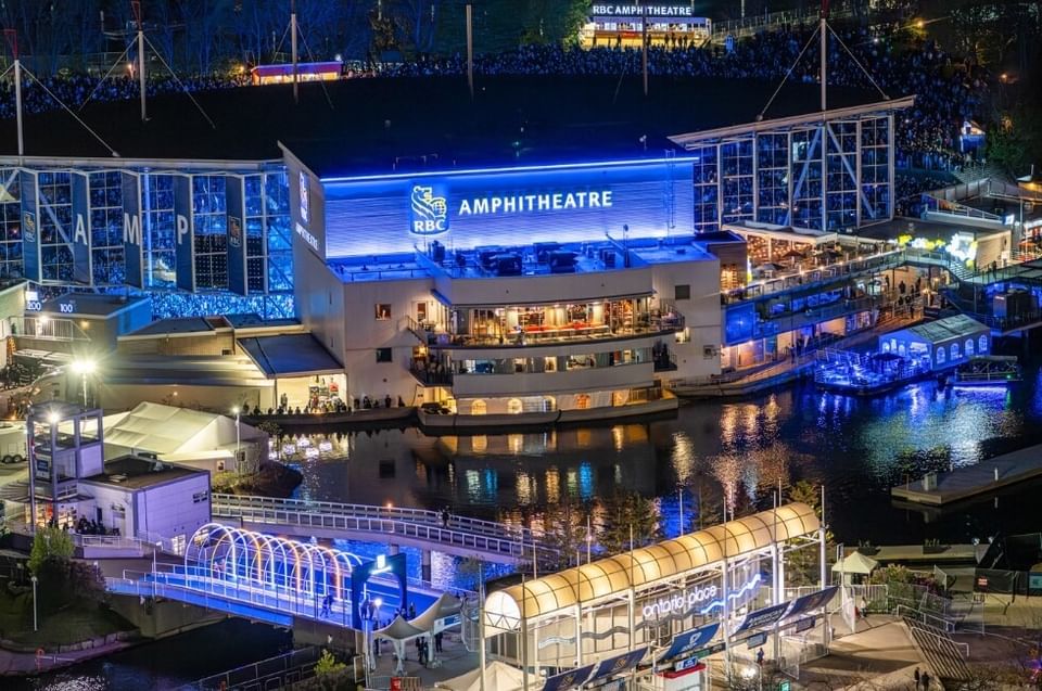 RBC Amphitheatre glowing by waterfront bridges and buildings under blue night lights near Hotel X Toronto