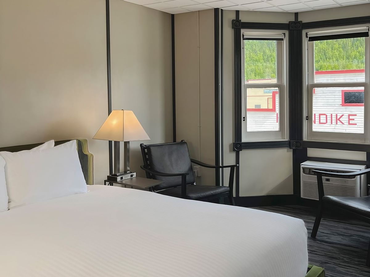 Hotel room with king bed, lamp, night stand, chair, and window
