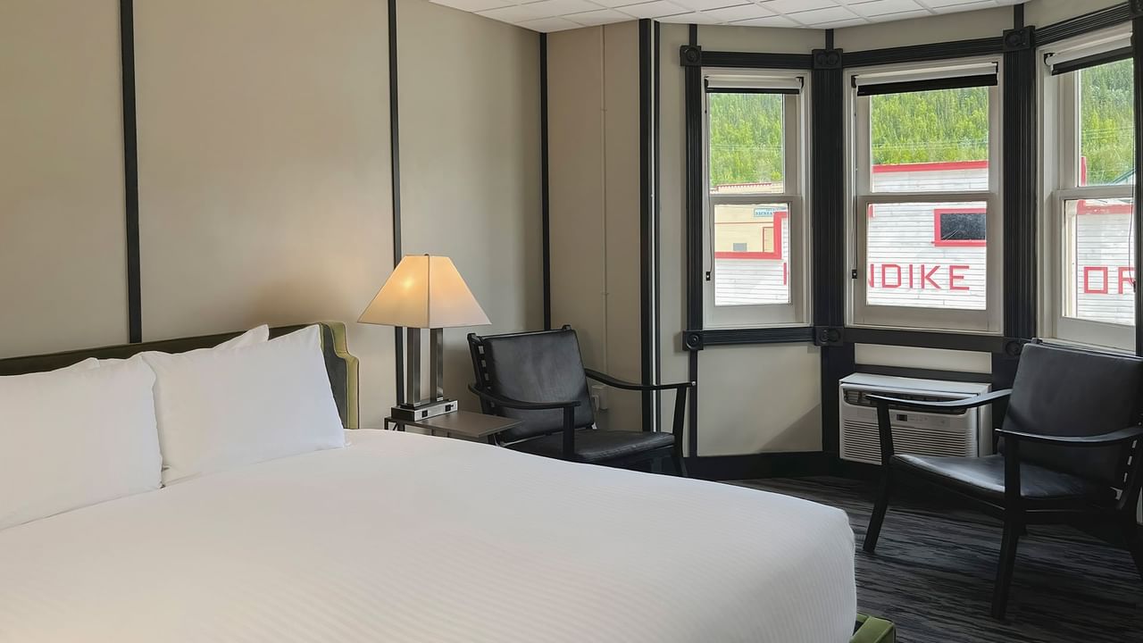 Hotel room with king bed, lamp, night stand, chair, and window