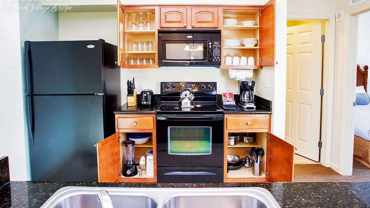 A kitchenette with black appliances, wood cabinets, and granite countertops.