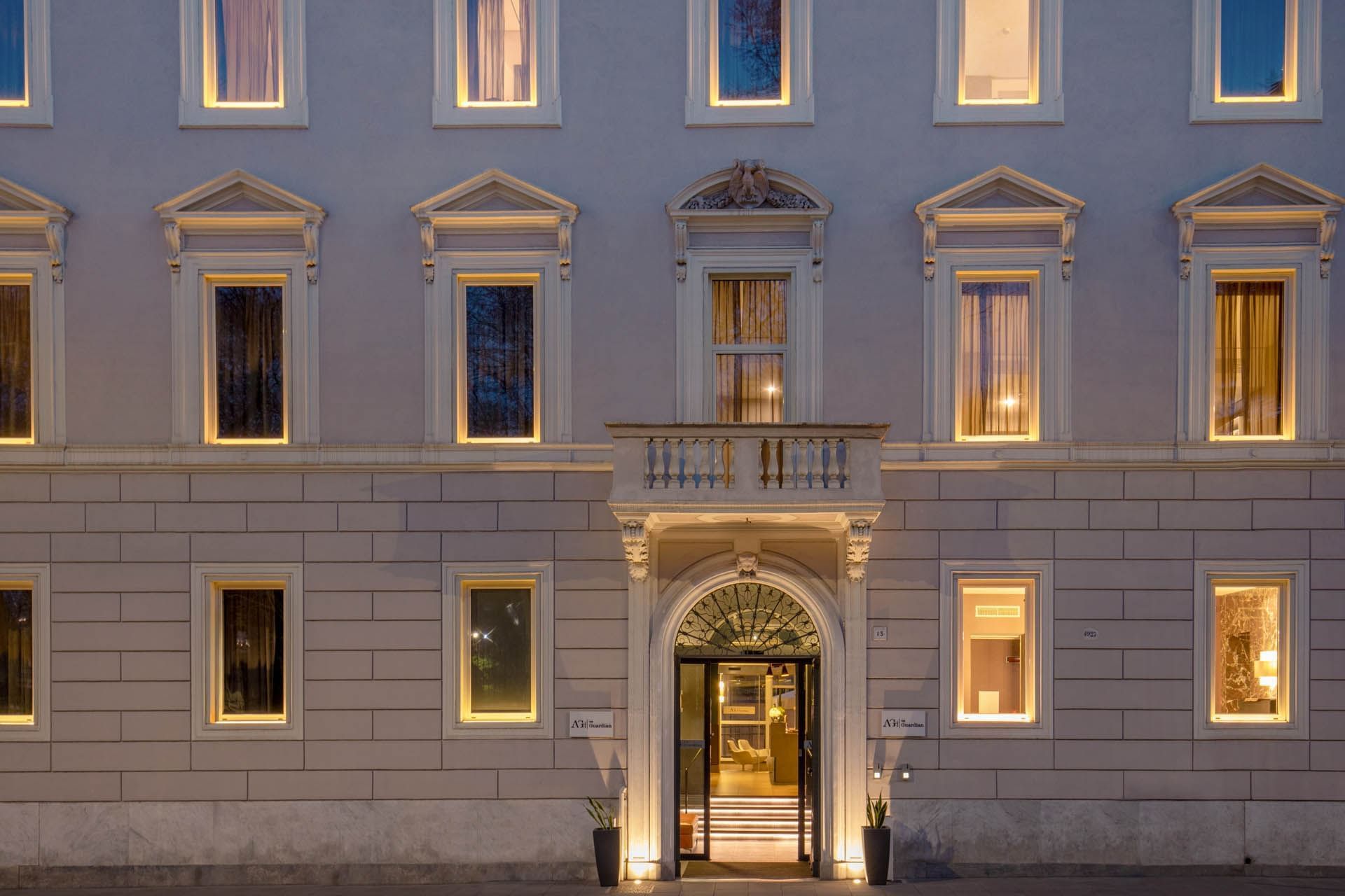 Elegant entrance of The Guardian Hotel with illuminated windows and a stylish doorway at dusk