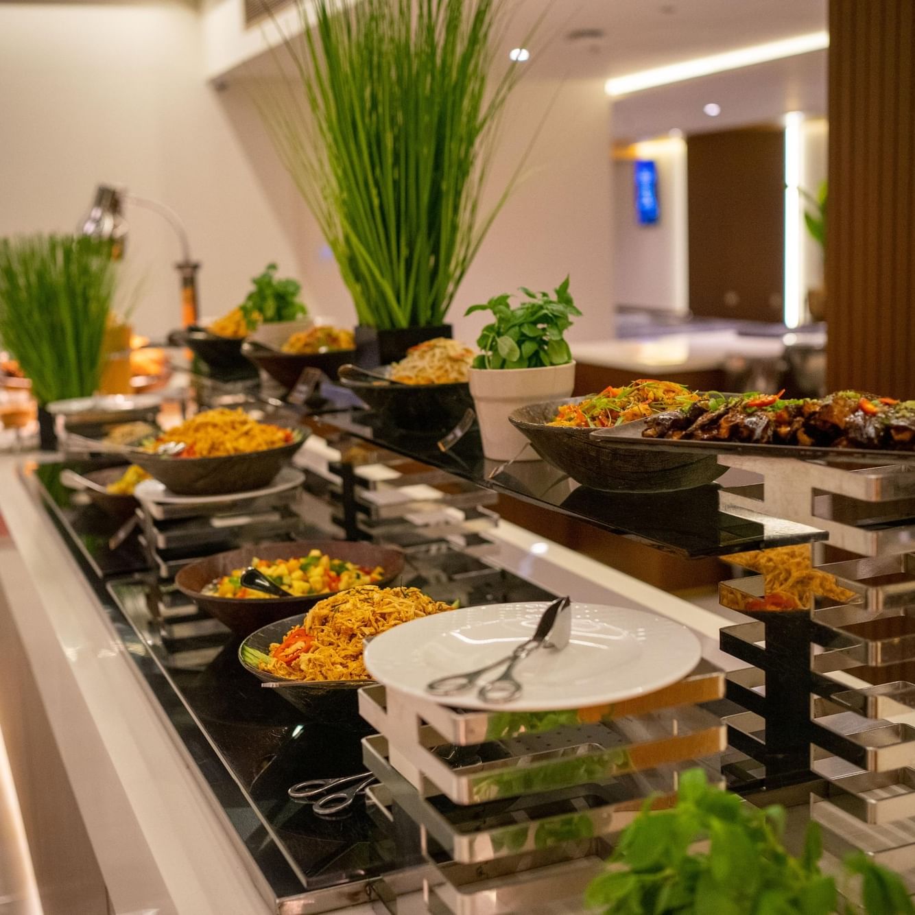 A buffet spread with various dishes, garnishes, and a plate with tongs on a sleek, modern dining setup.