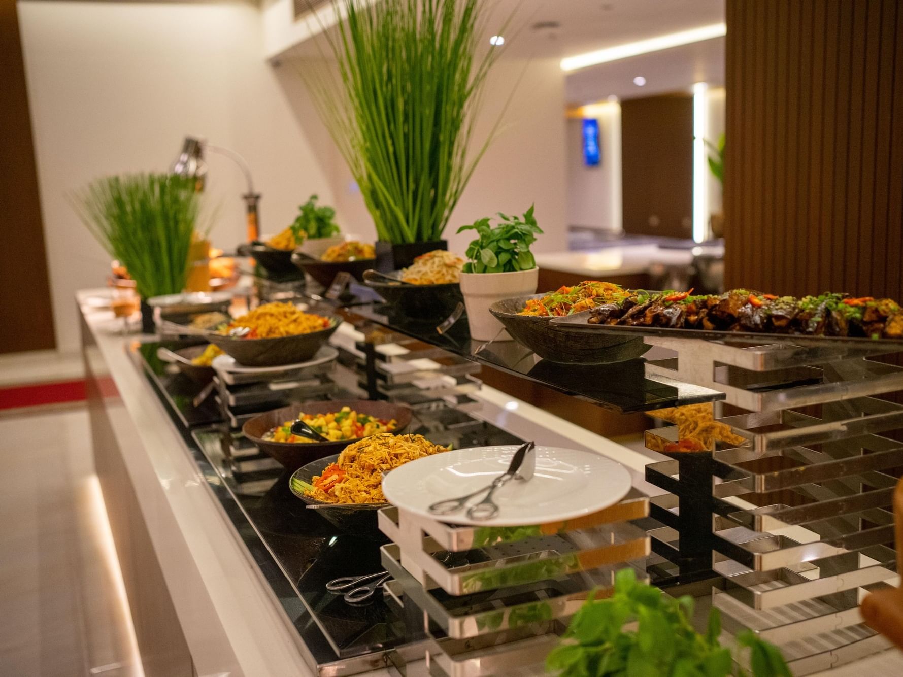 Ein Buffet mit verschiedenen Gerichten, Beilagen und einem Teller mit Zange auf einem schlichten, modernen Tisch.