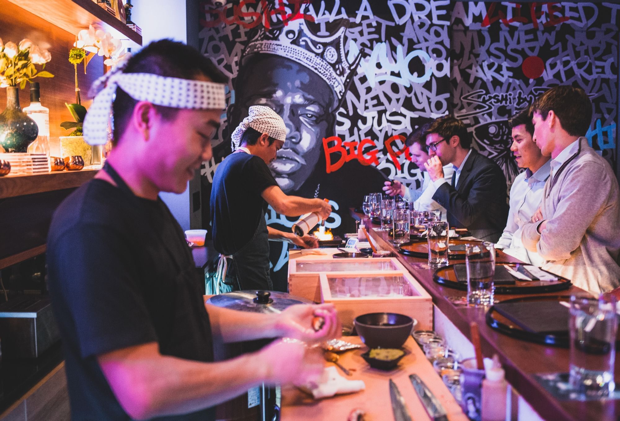 A bar with a bartender preparing food and customers seated at the counter