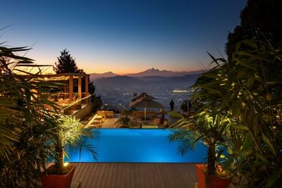 Rooftop pool with city lights and mountains at dusk at The Terraces Resort & Spa
