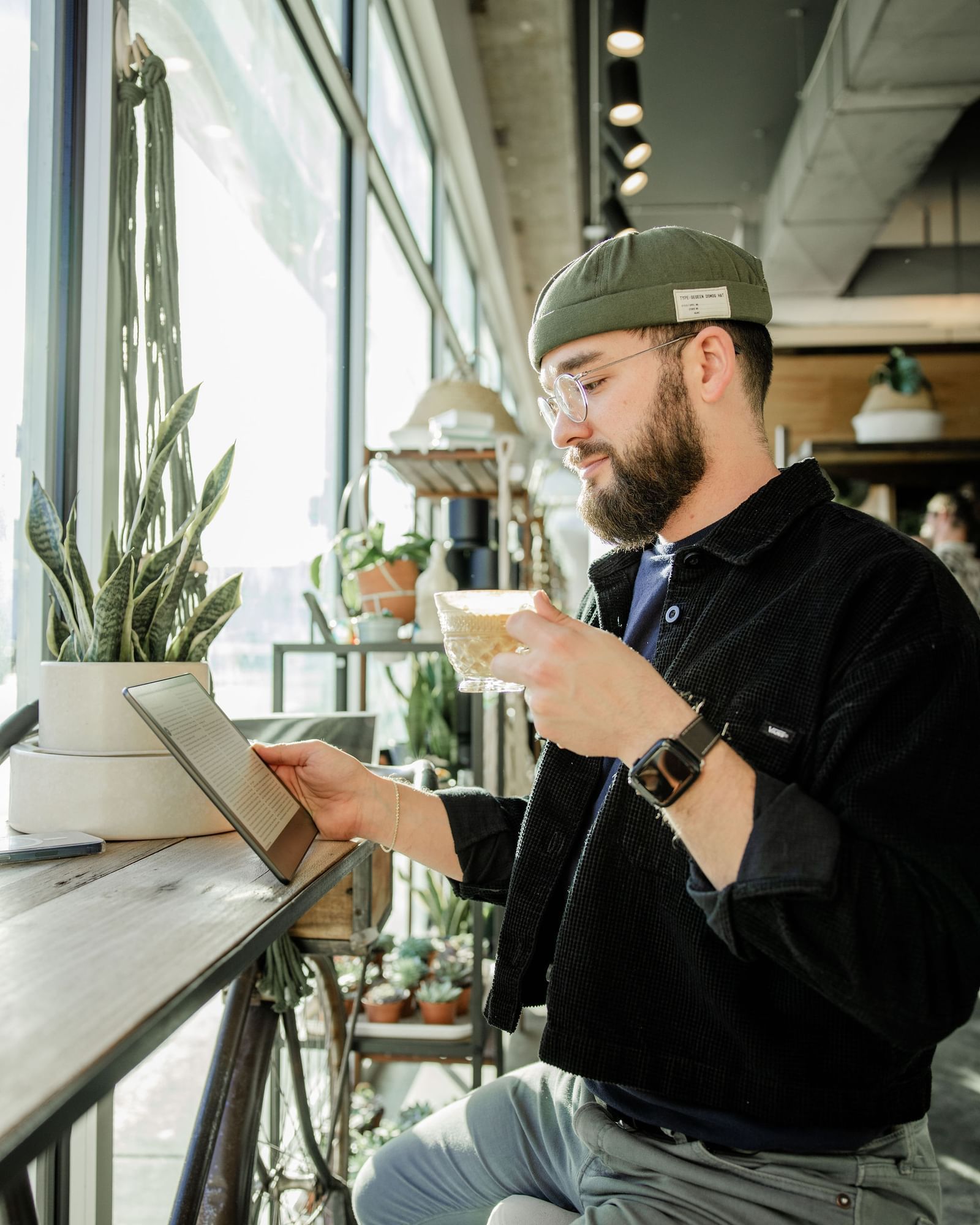 A man sits at a bar with a tablet and a cup.