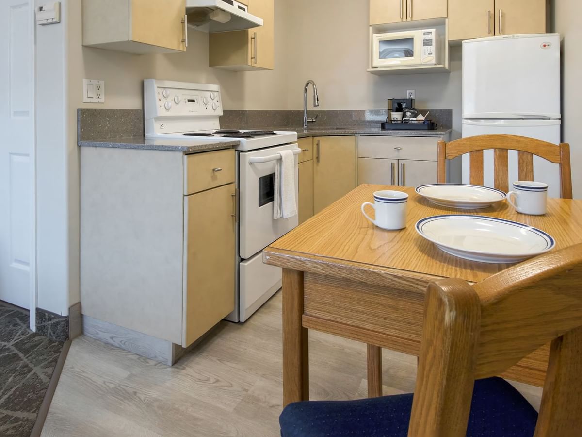 A cozy kitchenette setup with an oven, microwave, fridge, and a small dining table with plates and cups.