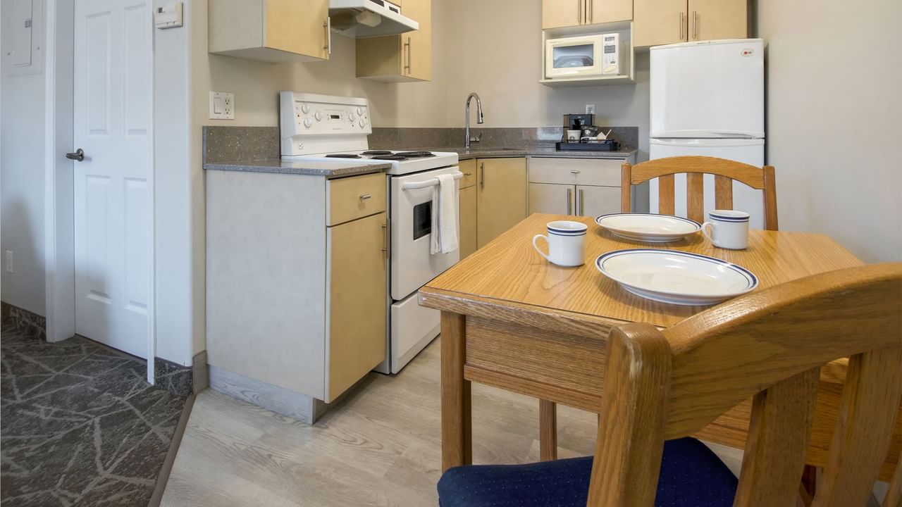 A cozy kitchenette setup with an oven, microwave, fridge, and a small dining table with plates and cups.