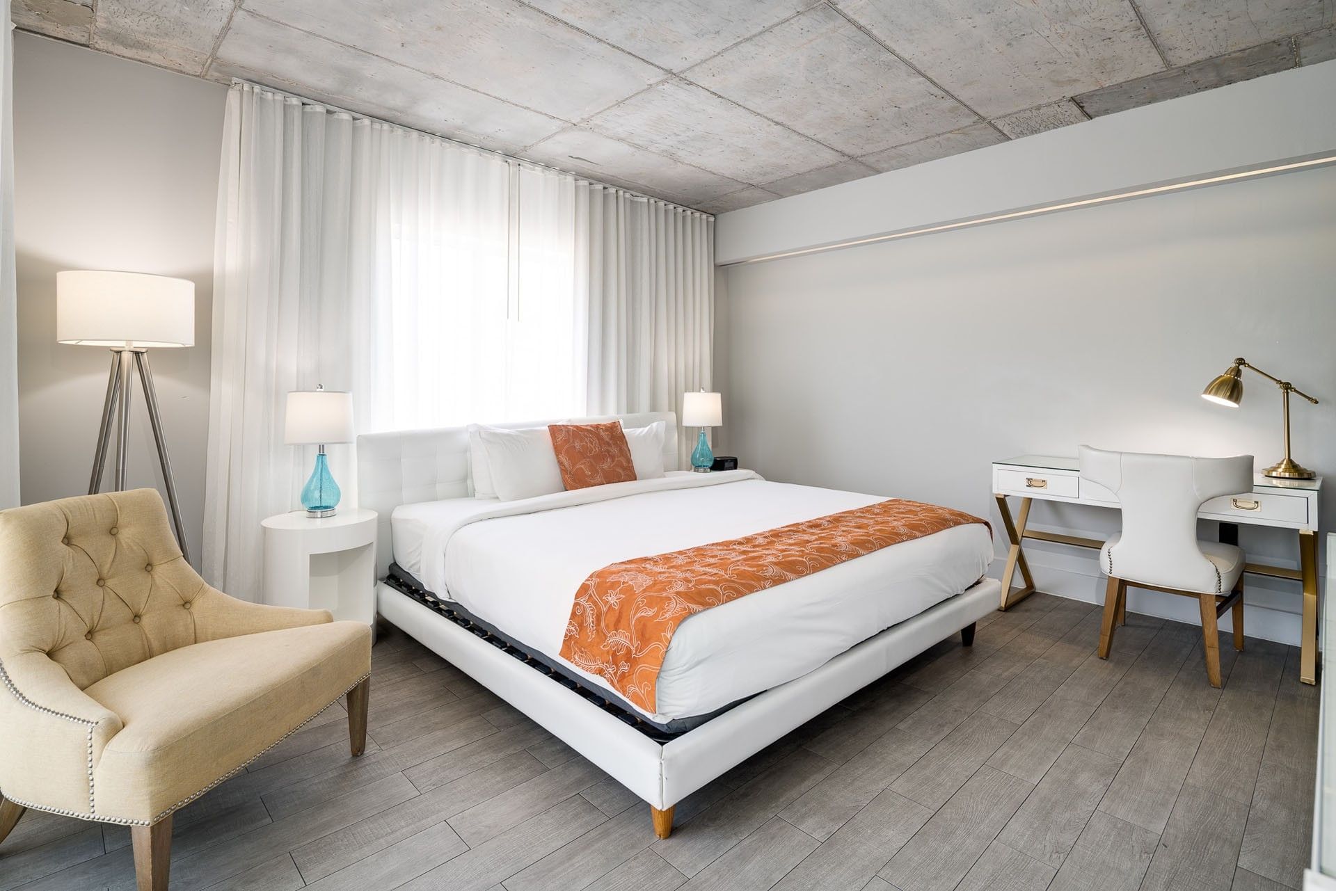 A hotel room with a king-size bed, desk, chair, and window