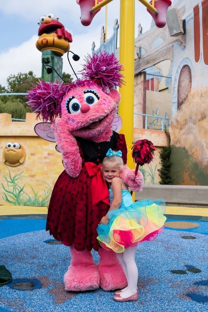 A young girl in a colorful tutu hugs Abby Cadabby in Sesame Street Land.