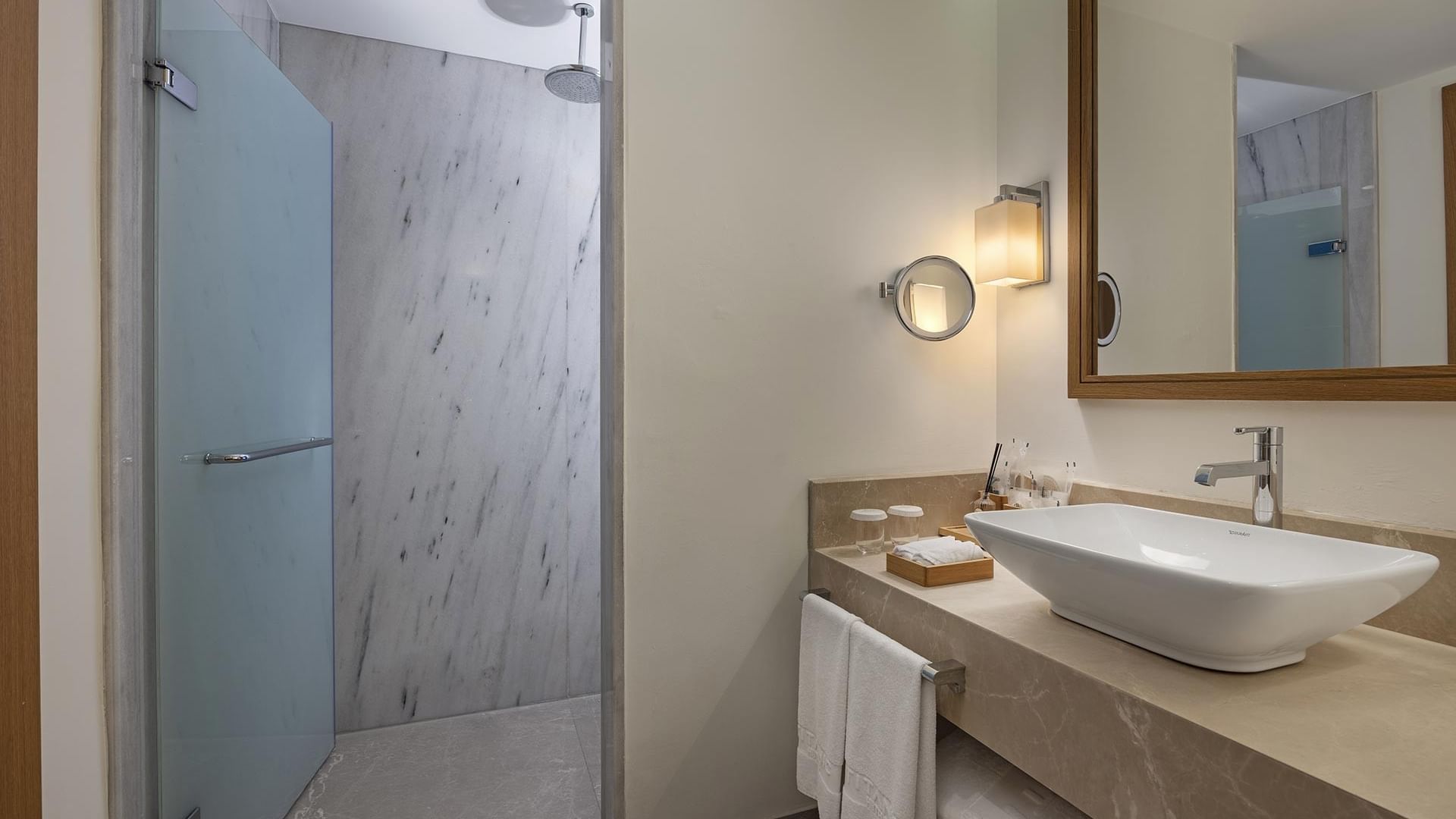 Geniş lavabolu, aynalı, cam kapılı duşakabinli ve mermer duvarlı banyo–Titanic Luxury Collection Bodrum.