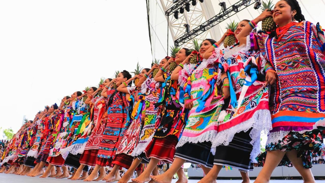 Women in vibrant embroidered dresses holding pineapples at a cultural event near Camino Real Pedregal Mexico