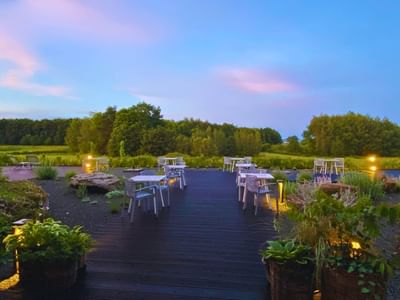 Outdoor dining with arranged tables on a wooden deck, surrounded by lush greenery and gentle lighting at Avaneo Hotel 
