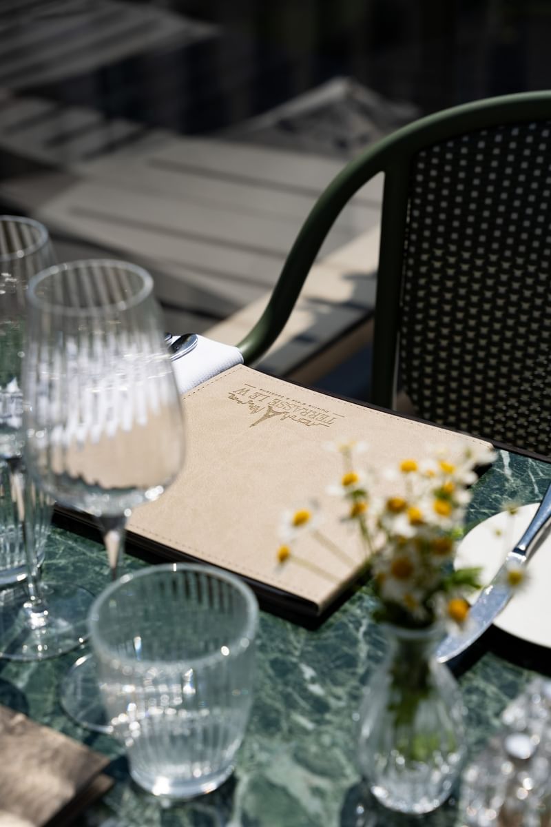 Outdoor table setting with glassware, menu, and white daisies beside a green woven chair at Warwick Paris Champs Elysées