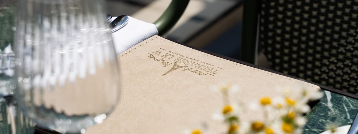 Table dressée avec menu, verres et fleurs sur la Terrasse Le W au Warwick Paris Champs-Elysées